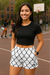 Woman standing on a basketball court wearing a black crop top and white shorts with black chain link pattern.
