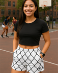 Woman standing on a basketball court wearing a black crop top and white shorts with black chain link pattern.