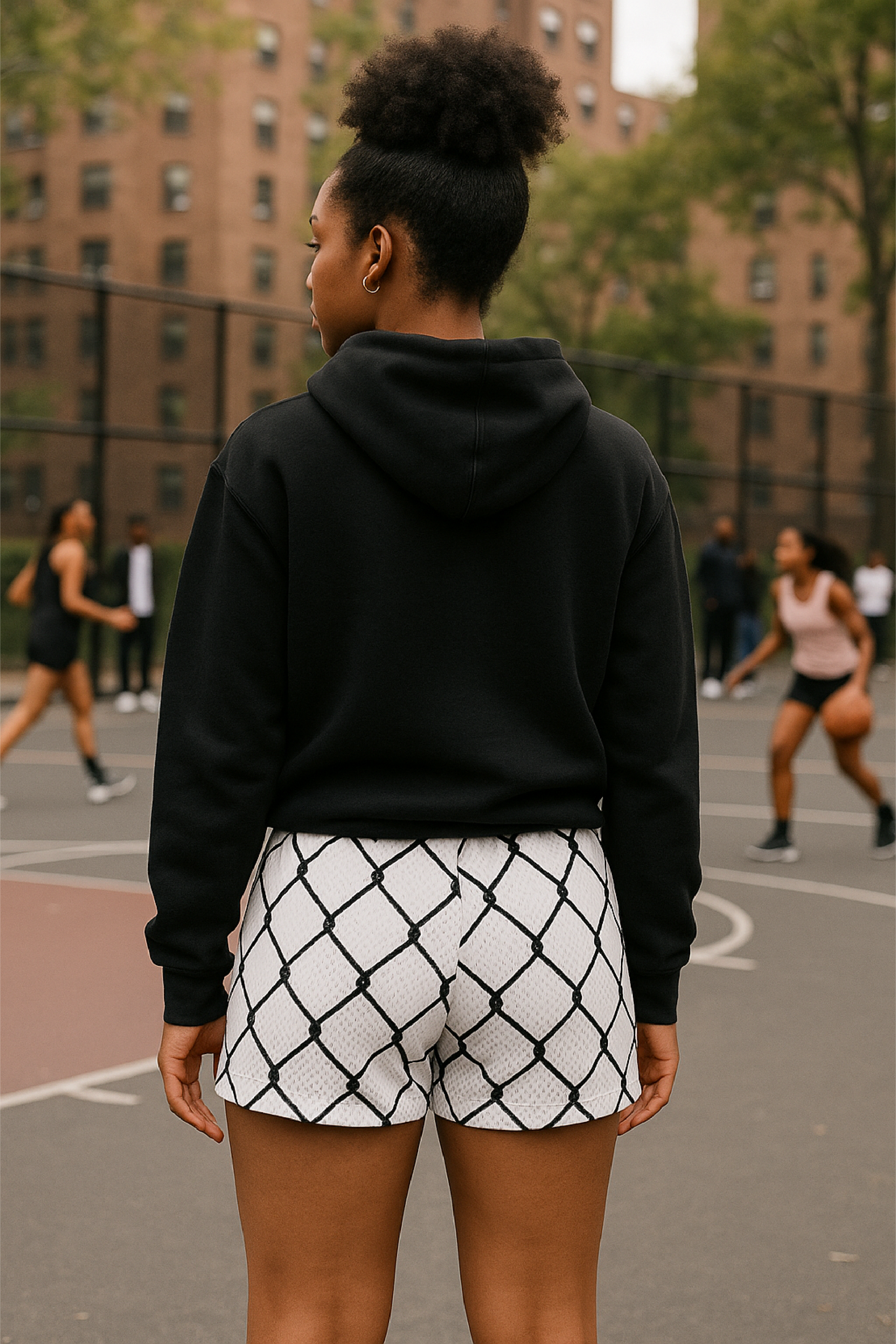 Person wearing a black hoodie and white shorts with black chain link pattern on a basketball court.