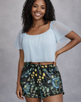 Woman Wearing a white top and RF-Wear Women's Floral 2.0 Shorts in Black/Blue/Yellow