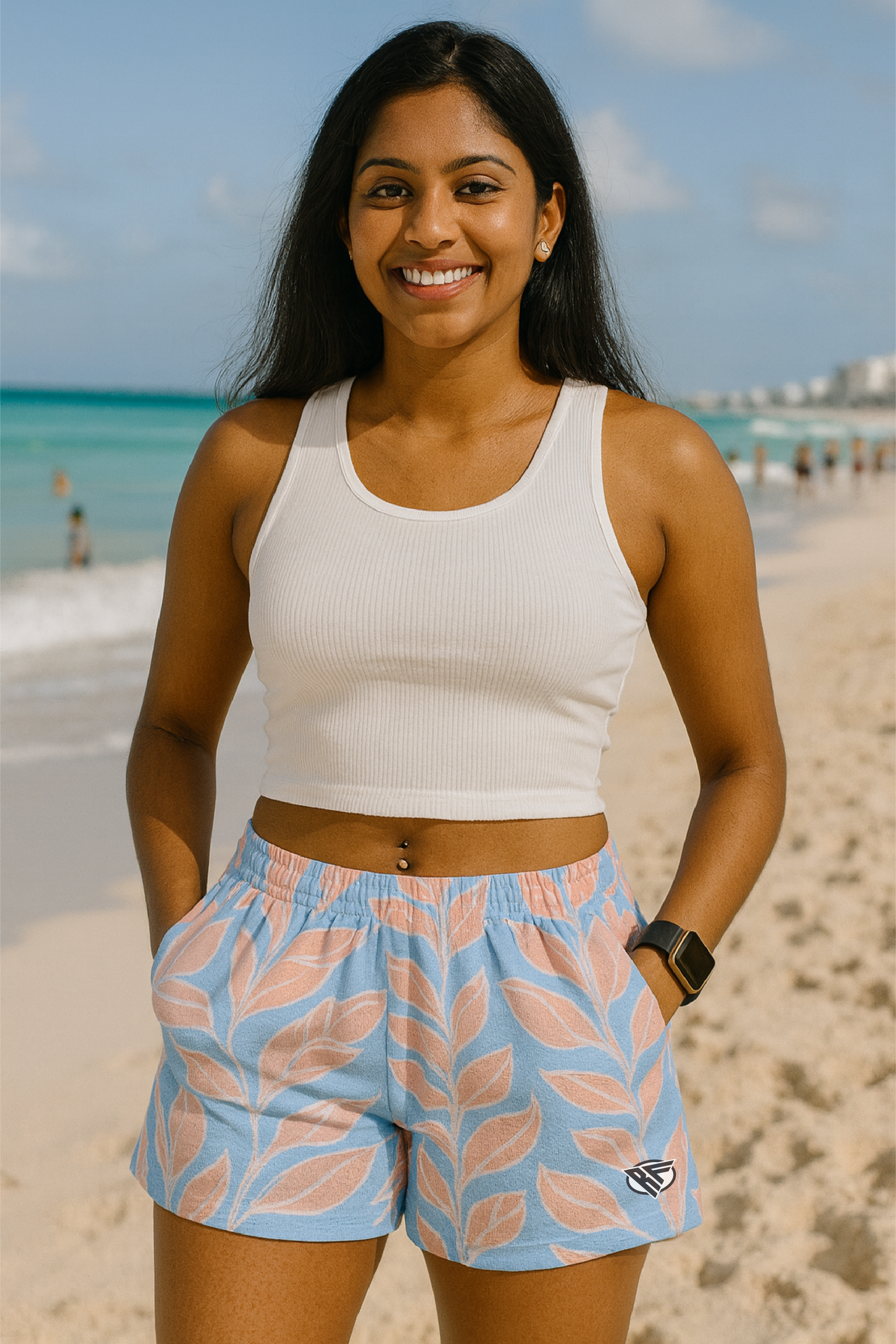 Woman in a white tank top and blue shorts with pink leaf pattern on a beach.