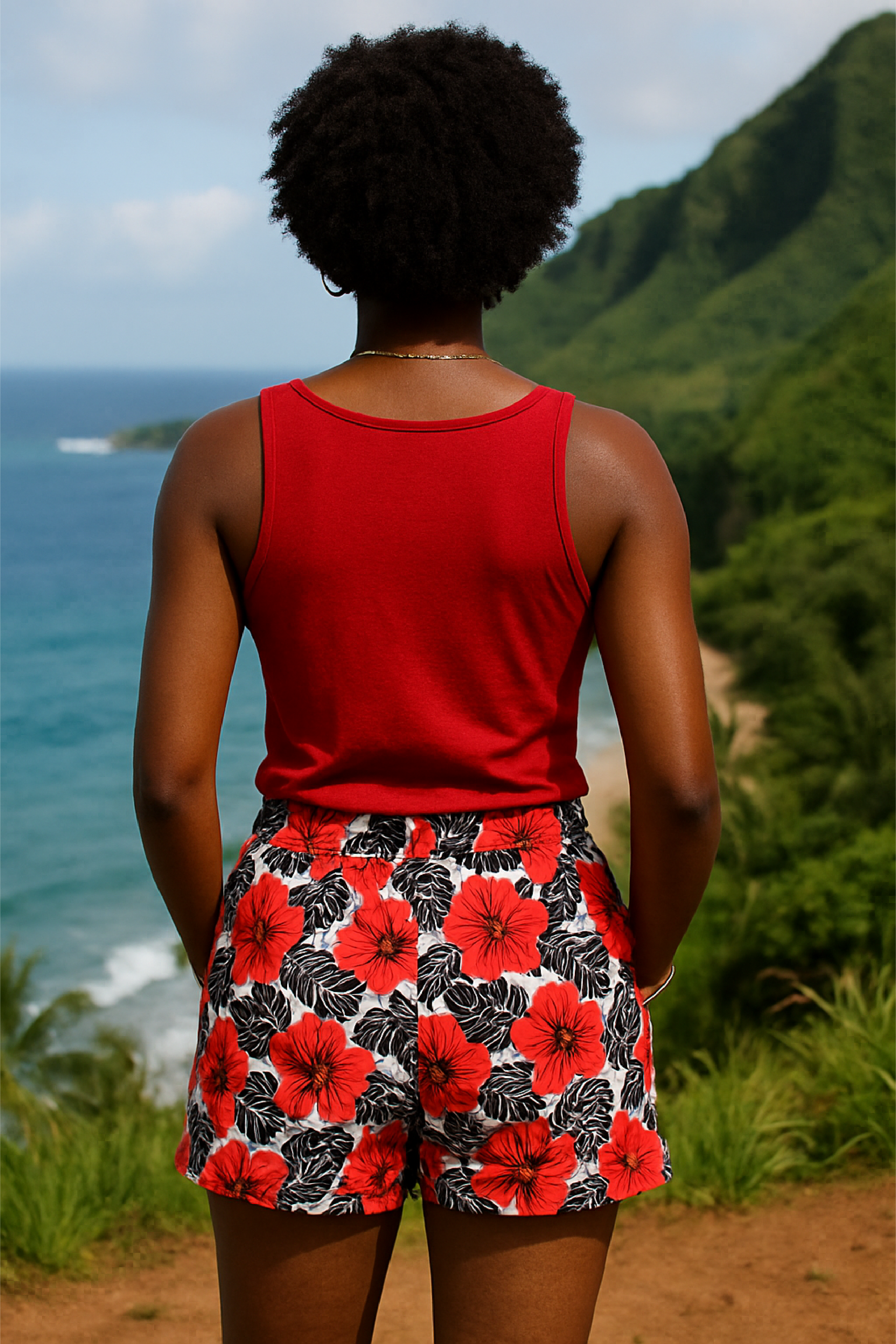 Person wearing a red tank top and floral shorts standing with their back to the camera, overlooking a scenic ocean view with mountains.
