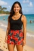 Woman wearing a black tank top and coral  on black white floral tropical shorts on a beach.