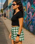 Woman wearing a black tank top and RF-Wear Houndstooth in green/white  shorts standing on a sidewalk with graffiti in the background.