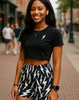 Woman wearing a black crop top with a lightning bolt design and black and white lightning bolt patterned shorts on a city street.