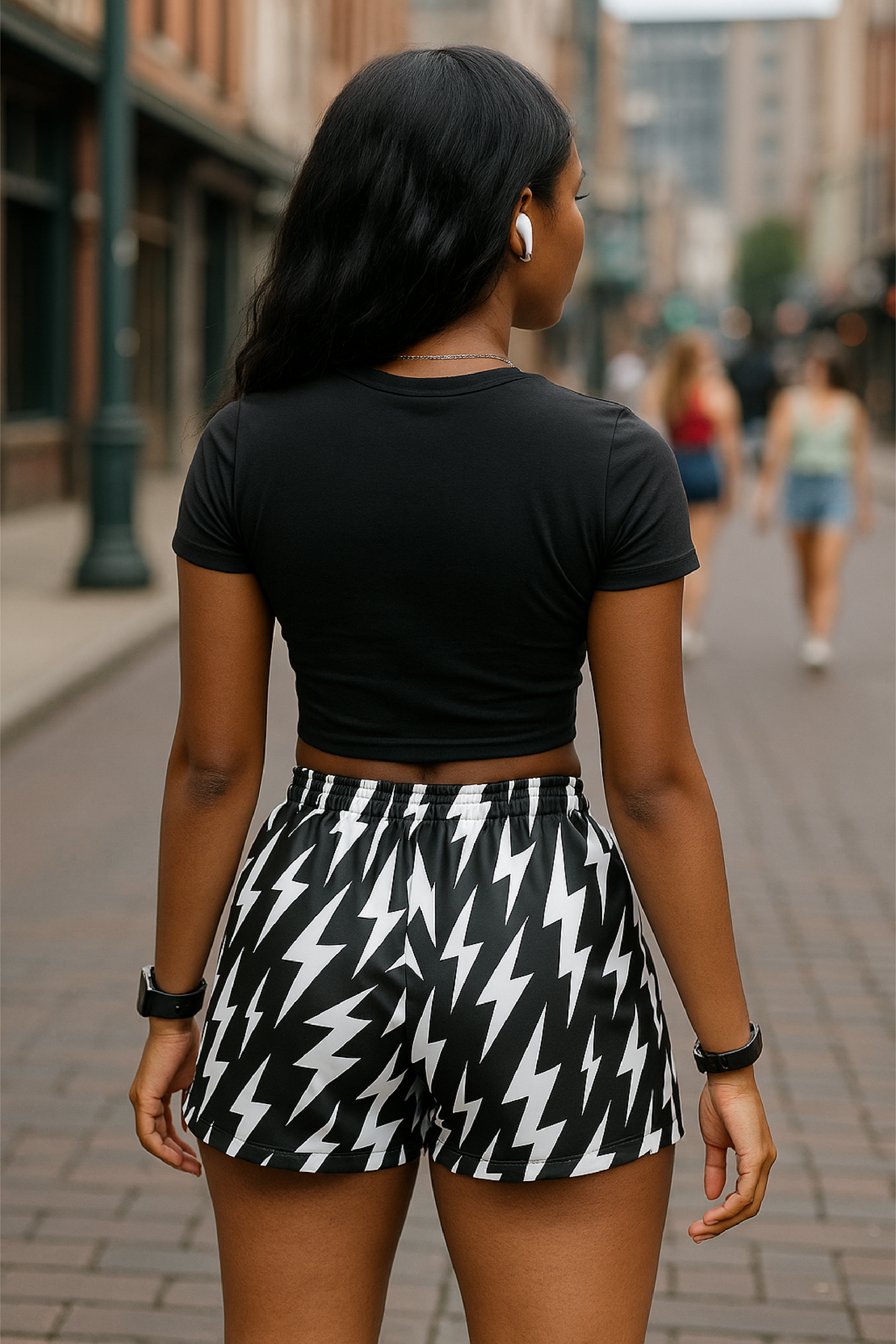 Woman wearing a black crop top with a lightning bolt design and black and white lightning bolt patterned shorts on a city street.