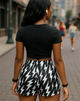Woman wearing a black crop top with a lightning bolt design and black and white lightning bolt patterned shorts on a city street.