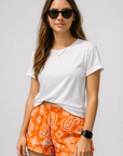 Woman wearing a white top and RF-Wear Women's Paisley Shorts in Orange/White 
