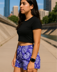 Woman standing on city sidewalk wearing RF-Wear Women's Paisley Shorts - Purple/White- Side View