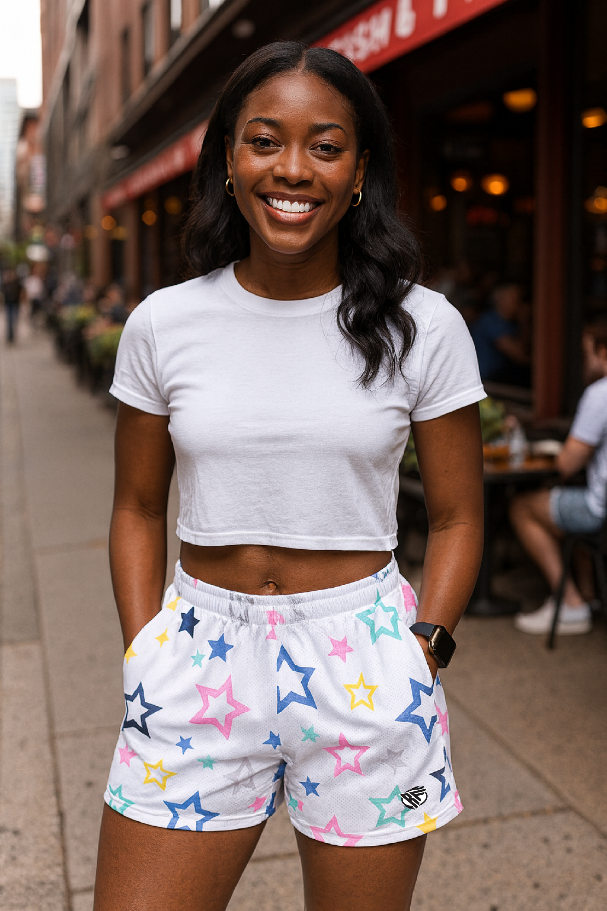 Woman wearing a white crop top and colorful star-patterned shorts on a city street.