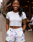 Woman wearing a white crop top and colorful star-patterned shorts on a city street.