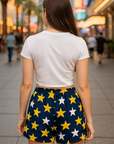 Person wearing a white t-shirt and star-patterned shorts on a city street.