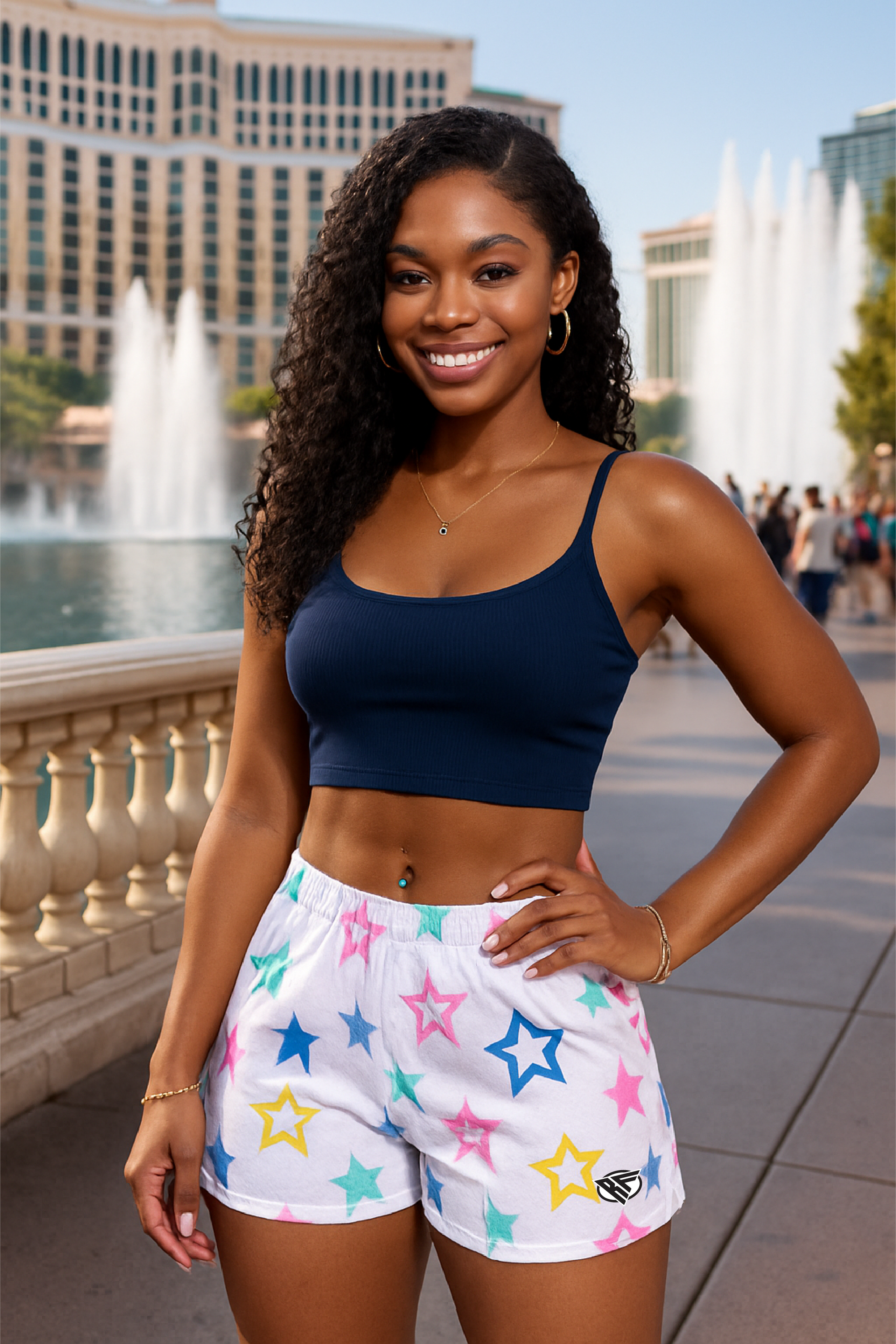 Woman wearing a blue sports bra and star-patterned shorts standing in front of fountains.