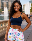 Woman wearing a blue sports bra and star-patterned shorts standing in front of fountains.