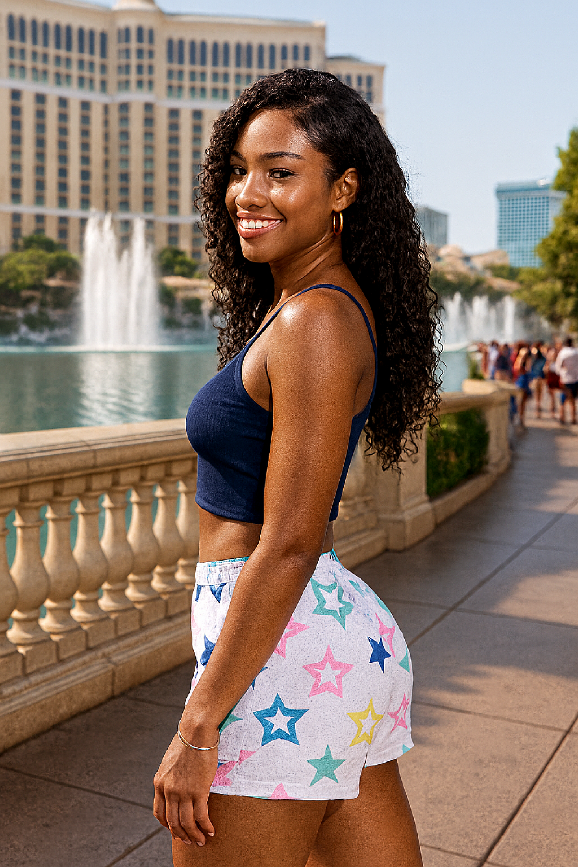 Woman in a blue top and colorful star shorts standing in front of a fountain and buildings.