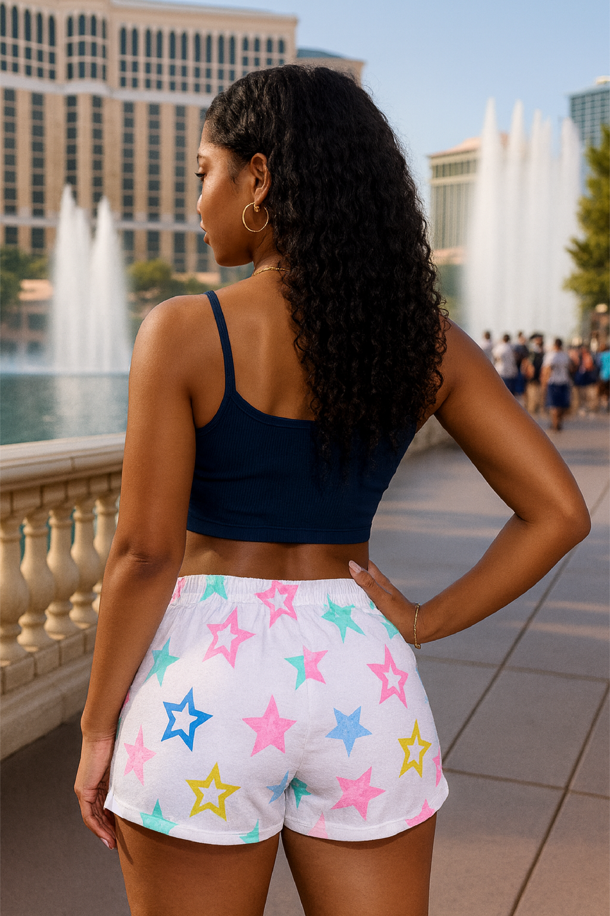 Woman wearing a navy crop top and colorful star-patterned shorts standing in front of fountains.