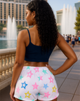Woman wearing a navy crop top and colorful star-patterned shorts standing in front of fountains.
