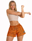 Woman wearing a beige top and RF-Wear Women's Tiger Shorts in orange/black.