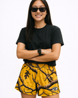 Woman wearing a black top and RF-Wear Women's Tree Camo Shorts in Yellow