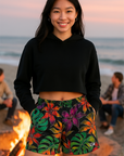 Woman wearing a black crop top and colorful floral shorts on a beach.