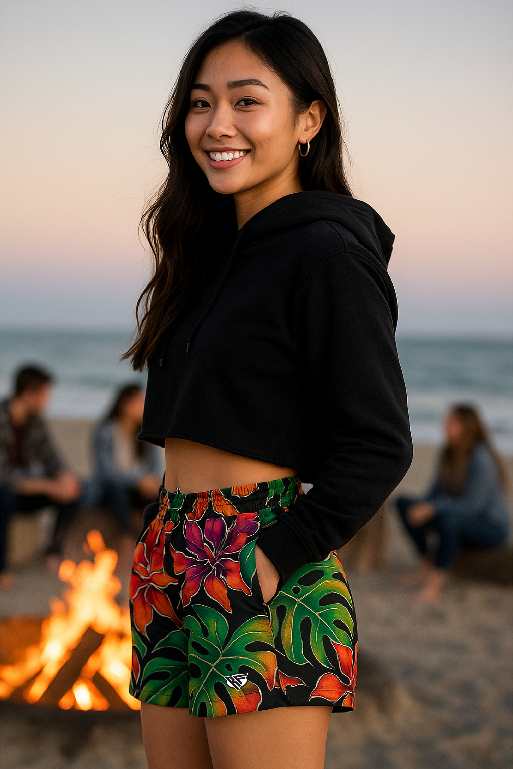 Woman in black crop top and colorful floral shorts standing on a beach.