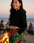 Woman in black crop top and colorful floral shorts standing on a beach.