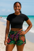 Woman in black cropped top and colorful shorts standing on the beach. 