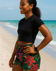 Woman in black cropped top and colorful shorts standing on the beach. 