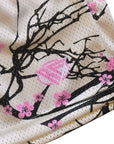Close-up of a fabric with black tree branches and pink blossoms on a cream background with brand logo