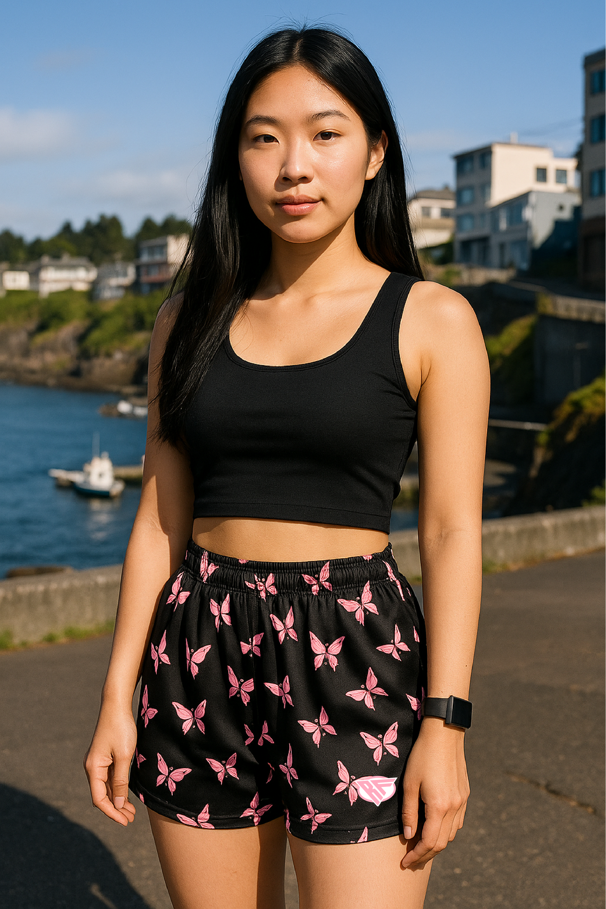 Woman standing near water with building in the background wearing a black crop top and RF-Wear Women's Butterfly Shorts in Black/Pink.