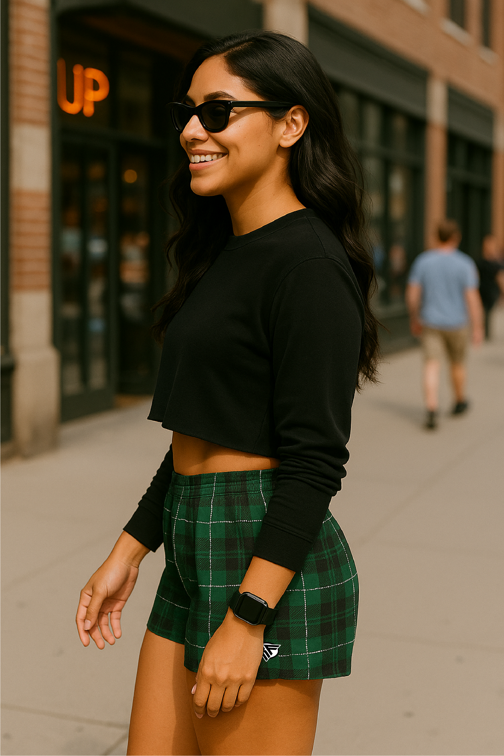 Woman wearing a black crop top and green plaid skirt on a city street.