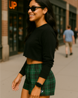 Woman wearing a black crop top and green plaid skirt on a city street.